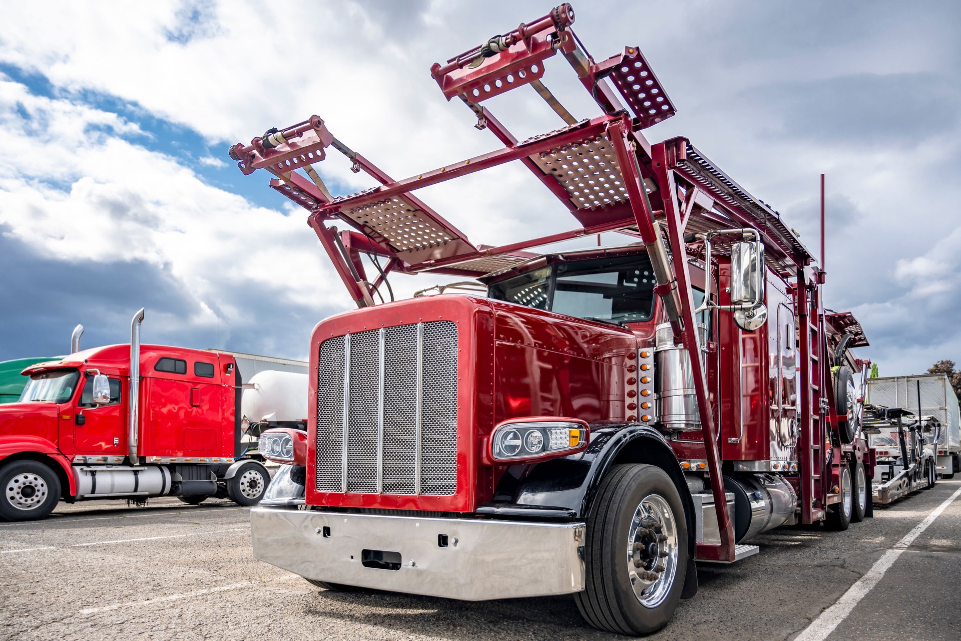 Dark red big rig car hauler semi truck with empty modular semi trailer standing on the industrial parking lot with another semi trucks